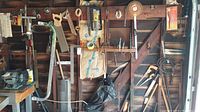Garage wall with saws, hammers, files, and other tools hanging for display and storage.