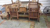 Four stacked and arranged wood patio pieces outdoors on a stone patio: three chairs and one double seat bench visible from front.