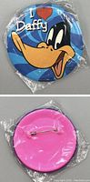 Front and back views of 1995 Warner Bros Looney Tunes I Love Daffy Duck button pin. Front shows colorful Daffy Duck graphic with text 'I ♥ Daffy'. Back is pink with metal safety pin for fastening. Pin is sealed in plastic packaging.