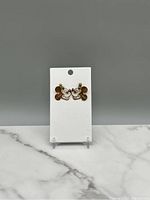 Pair of gold-tone Disney dangle earrings showing Mickey and Minnie Mouse faces touching noses on white card backing against gray background
