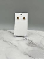 Pair of small round vintage gold tone stud earrings displayed on a white card against a gray background.
