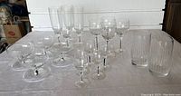 Assorted clear crystal glassware including wine glasses, parfait glasses, champagne flutes, aperitif glasses, tumblers, and a clear ribbed pitcher or ice bucket. Pieces feature dramatic black striping.