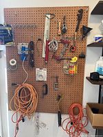Photo showing pegboard with multiple tools, two orange extension cords coiled, a can of Rust-Oleum spray paint, paint brushes, and various hardware hung on hooks.
