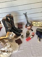 Photo showing mens cowboy boots size 10, wool scarf made in Germany, copper bellows, assorted small items including suspenders and a wallet, and white Tilley hat.
