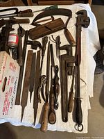 Overview of various vintage wooden and metal hand tools including files, wrenches, saws, and planes laid out on a white cloth