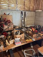 Wide view of workshop table with assorted tools and hardware scattered including different hand tools, electrical cords, and jars with nails and screws