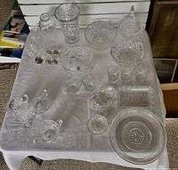 Top view of the entire crystal collection arranged on a white cloth, showing a variety of bowls, vases, glasses, and a covered dish.