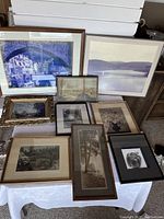 Group of nine framed art pieces displayed on table, showing variety of subjects and frame styles including antique frames