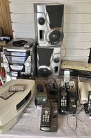 Full lot overview showing Sharp stereo system, Sony alarm clock, multiple Panasonic cordless phones, and slide magnifier.
