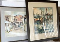 Two framed watercolor paintings by Hele Kowallek, one of an urban backyard scene and one of a harbor with boats.