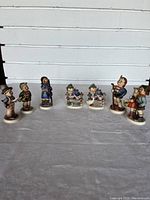 Wide shot of all seven Hummel figurines arranged in a row, showing various child character scenes including musical instruments and animals.