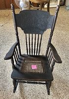 Full view of the antique kids rocking chair showing carved backrest, armrests, and cane seat.