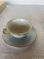 Close-up of a pale blue teacup with gold handle and floral pattern inside a matching saucer with gold rim.