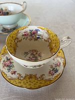 Close-up of yellow bordered teacup and saucer with detailed floral and gold trim