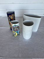 Four Rosenthal vases grouped on fabric surface showing diverse styles including two textured white ceramic and two colorful illustrated cylindrical vases.