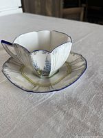 Side view of teacup on saucer showing octagonal shape, floral silver design, blue rim and handle.