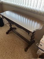 Side view of antique wooden side table showing scalloped edge tabletop, turned legs, and stretcher base.