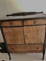 Front view of the antique cabinet showing two small top drawers, two cupboard doors in the middle, and a large bottom drawer. Ornate carved detail on top.