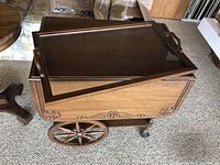 Side view of wooden bar cart showing carved detailing and spoked wheel.