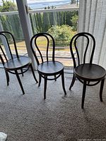 Three wooden bentwood chairs shown near window, dark wood finish.