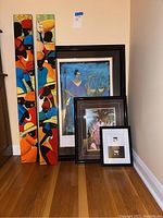 Full view of all five artworks: two long colorful canvas pieces, and three framed prints leaning against the wall.