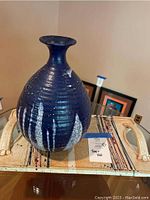 Close side view of blue/black ridged art pottery jar on the ceramic tray showing white vertical drip glaze