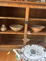 Two stone bowls displayed inside wooden cabinet, small pottery vase also visible