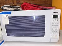 Front view of white Panasonic microwave with oven mitts and aprons on top