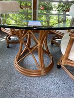 Side view showing light brown rattan construction with tightly wrapped bindings and circular rattan frame supporting thick clear glass top.