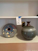 Side by side photo of both art pottery vases on a shelf, showing overall shapes and designs