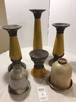 Three yellow Fitz and Floyd candle sticks with dark ribbed bases and tops accompanied by two glass cloches on metal bases, showing all items from an angled front view.