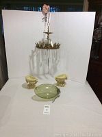 Full shot showing all three items in the set: cream urn bookends, hanging glass vase, and metal and acrylic chandelier suspended above.