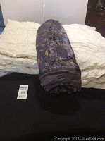 Three bedding items laid out: a queen down comforter, a twin down comforter, and a rolled-up queen-sized bamboo print duvet cover in dark silky fabric with bamboo leaf designs.