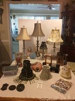 Photo showing four table lamps with varying decorative fabric shades, two wooden picture frames, a glass ombre candle holder, and small decorative items on a table.