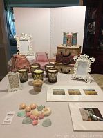 Overview photo showing prints, frames, candles, soaps, and decorative suitcases arranged on table.