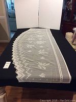 Full length view of the unfinished valance laid out on black fabric with scalloped lace edging and Lily of the Valley floral design.