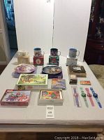 Photo showing Disney mugs, boxed puzzles, trading cards, commemorative plates, and Disney watches on a table.