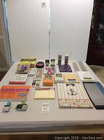 Wide view of lot items including paper trimmer, label maker, books, stamps, washi tape, and other paper crafting supplies laid out on table.