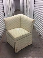 Front view of upholstered corner chair showing hexagonal patterned fabric and skirted base.