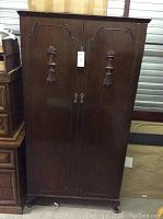 View of the closed armoire showing dark wood finish, decorative door carvings and handles.