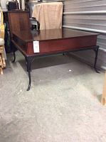 Square coffee table with metal legs, wooden top and two drawers with ring handles shown from side angle.