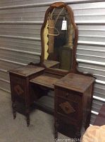 Front view of antique wooden vanity with mirror and two side drawers, showing carved details and overall condition.