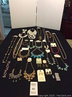 Full view of assortment of costume jewelry laid out on black cloth, showing various necklaces, bracelets, and earrings.