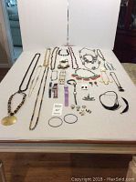 Photo showing the full spread of assorted costume jewelry on a table, various necklaces, rings, bracelets, watches, and earrings visible.