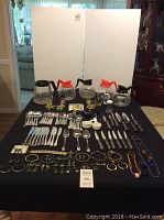 Full lot on black tablecloth showing silverware, costume jewelry, coffee pots, knives, toys, and mug