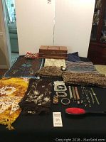 Wide photo showing wooden jewelry box at back with fashion scarves and knit hat and scarf laid out on a table.