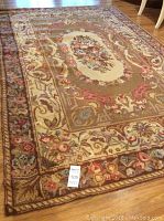 Full view of rectangular wool rug showing the overall petit point floral pattern and border in multiple earthy tones on hardwood floor.
