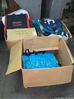 Box with assorted hobby bags including an Office Depot bag, blue and purple tote bags, and teal duffel bags.