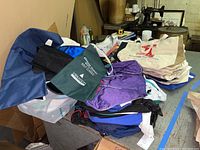 Overview of assorted bags including canvas tote bags, golf ball bags, and duffel bags arranged on a surface.