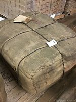 Photo showing a tightly bundled large rectangular stack of burlap bags bound with black straps on a wooden pallet.